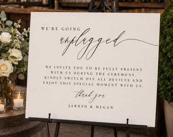 Pode incluir: Uma placa de casamento retangular branca num cavalete de metal preto com texto preto que diz: WE'RE GOING unplugged WE INVITE YOU TO BE FULLY PRESENT WITH US DURING THE CEREMONY. KINDLY SWITCH OFF ALL DEVICES AND ENJOY THIS SPECIAL MOMENT WITH US. thank you JARRED & MEGAN