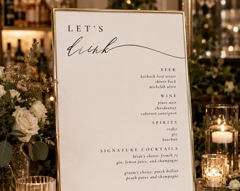 Pode incluir: Uma placa retangular com moldura dourada e fundo branco apresentando o texto LET'S drink em letras pretas. O menu lista cerveja, vinho, destilados e coquetéis exclusivos, incluindo bride's choice french 75 e groom's choice peach bellini.