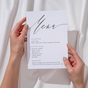 Puede incluir: Una tarjeta de menú rectangular blanca con texto negro que presenta la palabra Menu en una fuente cursiva en la parte superior. El menú enumera secciones para Starter, Pasta Bar y Dessert con platos como garlic knots, ravioli y wedding cake.