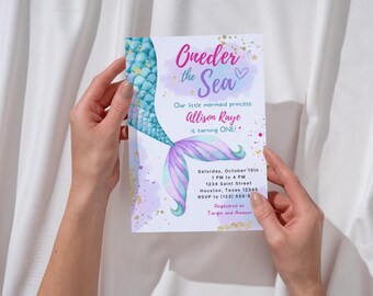 Pode incluir: Um convite de aniversário com tema de sereia, segurado por uma pessoa. O convite apresenta o texto "Oneder the Sea" e "Our little mermaid princess Allison Raye is turning ONE!" O convite tem um design de cauda de sereia em tons de azul, roxo e verde.