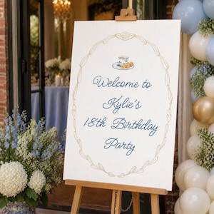 Peut inclure: Un chevalet en bois supporte une affiche blanche avec l'inscription "Welcome to Kylie's 18th Birthday Party" en bleu marine, encadrée d'un motif floral doré et d'une illustration de tasse à thé. La scène comprend des compositions florales et des ballons.