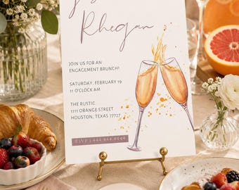 Pode incluir: Um convite para um brunch de noivado com os nomes "Josh + Rhegan" em escrita elegante. O convite apresenta taças de champanhe em aquarela e o texto "Join us for an engagement brunch!" em uma mesa com doces, frutas e flores.