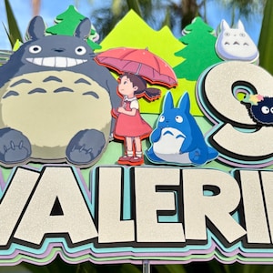 May include: A colorful cake topper featuring characters from the animated film "My Neighbor Totoro." The design includes the characters Totoro, Mei, and the Catbus, along with the name "VALERIE" in large, layered letters. The number "9" is also included.
