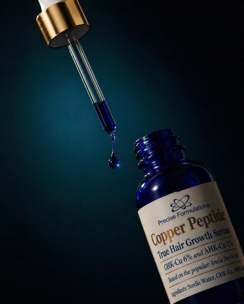 May include: A blue glass bottle of Precise Formulations Copper Peptide True Hair Growth Serum with a gold-capped dropper. A single drop of the dark blue liquid is suspended from the glass pipette, positioned above the open bottle neck.