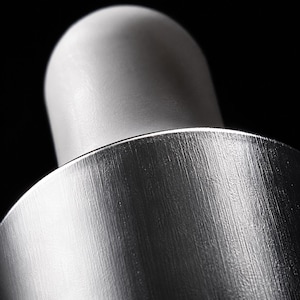 K&ouml;nnte beinhalten: Eine Nahaufnahme eines Pipettenaufsatzes mit einem glatten, matten wei&szlig;en Gummiball, der an einem zylindrischen Kragen aus geb&uuml;rstetem silbernem Metall befestigt ist. Die Metalloberfl&auml;che zeigt eine feine vertikale Maserung.