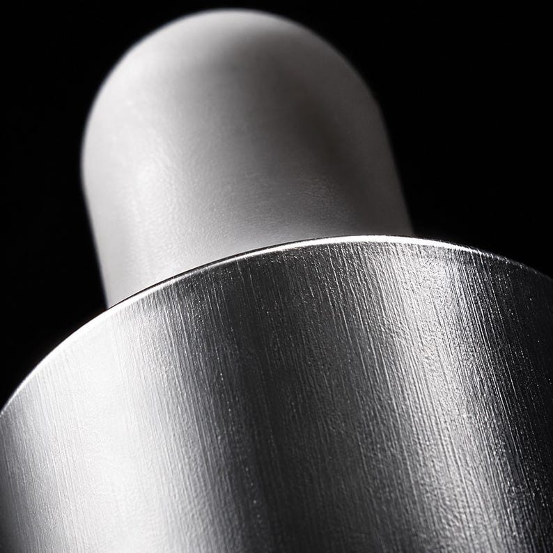 K&ouml;nnte beinhalten: Eine Nahaufnahme eines Pipettenaufsatzes mit einem glatten, matten wei&szlig;en Gummiball, der an einem zylindrischen Kragen aus geb&uuml;rstetem silbernem Metall befestigt ist. Die Metalloberfl&auml;che zeigt eine feine vertikale Maserung.