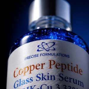 K&ouml;nnte beinhalten: Eine klare Glasflasche mit einem leuchtend blauen fl&uuml;ssigen Serum. Das wei&szlig;e Etikett tr&auml;gt den Text Precise Formulations, Copper Peptide Glass Skin Serum und GHK-Cu 3.33% in blauer und kupferfarbener Schrift, gekr&ouml;nt von einer silbernen Pipettenkappe.