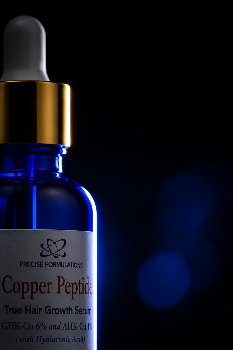 May include: A blue glass dropper bottle with a gold collar and white dropper top. The label reads PRECISE FORMULATIONS Copper Peptide True Hair Growth Serum GHK-Cu 6% and AHK-Cu 1% (with Hyaluronic Acid) with a circular atom-like logo above.