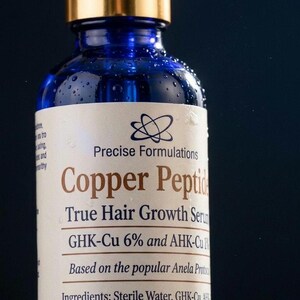 May include: A blue glass dropper bottle with a gold cap containing Copper Peptide True Hair Growth Serum. The label features the text Precise Formulations, GHK-Cu 6% and AHK-Cu 1%, and lists ingredients including Sterile Water, GHK-Cu, and AHK-Cu.