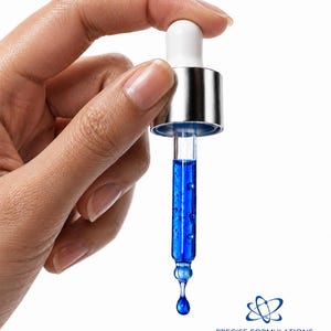 K&ouml;nnte beinhalten: Eine Glastropfpipette gef&uuml;llt mit einer leuchtend blauen Fl&uuml;ssigkeit, mit einem wei&szlig;en Gummisauger und einer silbernen Metallmanschette. Ein einzelner Tropfen des blauen Serums h&auml;ngt an der Spitze. Das Logo PRECISE FORMULATIONS ist unten zu sehen.