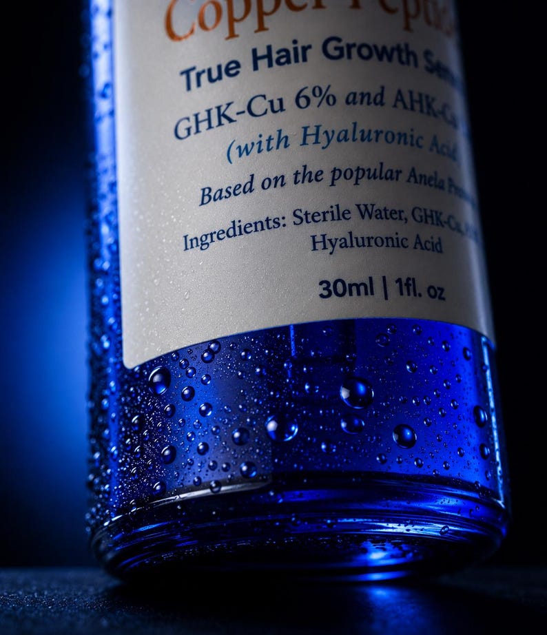May include: A blue glass bottle of Copper Peptide True Hair Growth Serum with a white label. The label lists GHK-Cu 6% and AHK-Cu, Hyaluronic Acid, and ingredients including Sterile Water. The bottle contains 30ml or 1 fl. oz and is covered in water droplets.