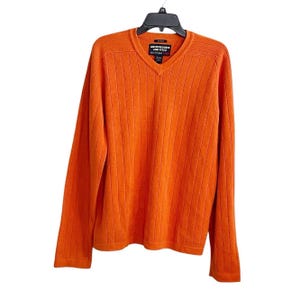 May include: A bright orange long-sleeve sweater with a V-neckline and vertical ribbed texture. The garment features a black label at the inner neckline with the white text Abercrombie and Fitch and a small red square logo.