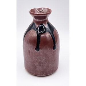 Pode incluir: Um vaso de cerâmica feito à mão com um corpo arredondado e um pescoço estreito. O vaso é principalmente de uma cor castanho-avermelhada suave, com esmalte preto pingando do topo. O vaso tem um acabamento brilhante e é provavelmente usado para fins decorativos.