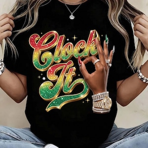 Puede incluir: Una camiseta negra con un estampado gráfico que muestra el texto "Clock It" en una fuente con degradado brillante en rojo, amarillo y verde. El diseño incluye una mano haciendo un gesto de "OK", adornada con varias pulseras plateadas y un reloj dorado.