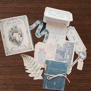 May include: A collection of paper ephemera including a book titled Secrets in the Library Drawer, a Reader's Ledger book, a Great Western Railway ticket, a fern leaf cutout, a vintage key, a child's house drawing, and a black and white photo print.
