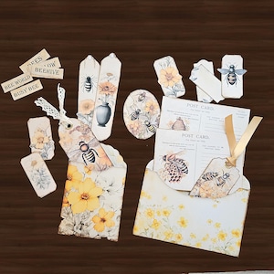 May include: A collection of bee-themed stationery items, including tags, postcards, and an envelope. The designs feature watercolor illustrations of bees, flowers, and a beehive, with text that reads "Bee World" and "Busy Bee".