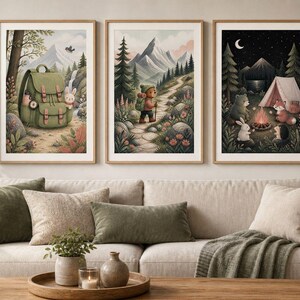May include: Three framed wall art prints displayed above a beige sofa. The left print shows a green backpack in a forest. The centre print depicts a bear hiking on a mountain trail. The right print features a bear, rabbit, and fox camping at night.