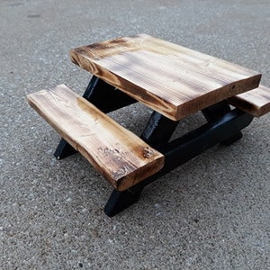 May include: A small wooden picnic table with black painted legs and a natural wood finish. The table has two benches.