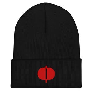May include: A black beanie hat featuring a red embroidered emblem. The emblem is a vertical line through an oval shape. The hat is made of a soft, knitted material and has a folded brim.