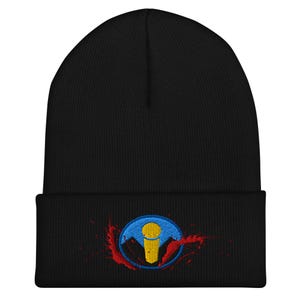 May include: Black beanie hat featuring an embroidered design of a yellow microphone within a blue circle, set against a red splatter effect. The beanie is made of a knitted fabric, suitable for colder weather.