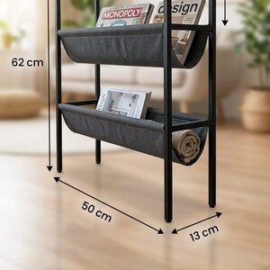 Op de afbeelding: Een zwart metalen en houten rek met twee grijze canvas planken en een natuurlijk grenen blad. De unit is 62 cm hoog, 50 cm breed en 13 cm diep. De bovenste plank bevat een kleine plant en een vergrootglas. De planken bevatten boeken.