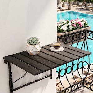 May include: A wall-mounted balcony table featuring a dark wood slat surface and a black metal frame. A white and gold geometric succulent planter sits on the table next to a glass coffee mug resting on a small white marble coaster.
