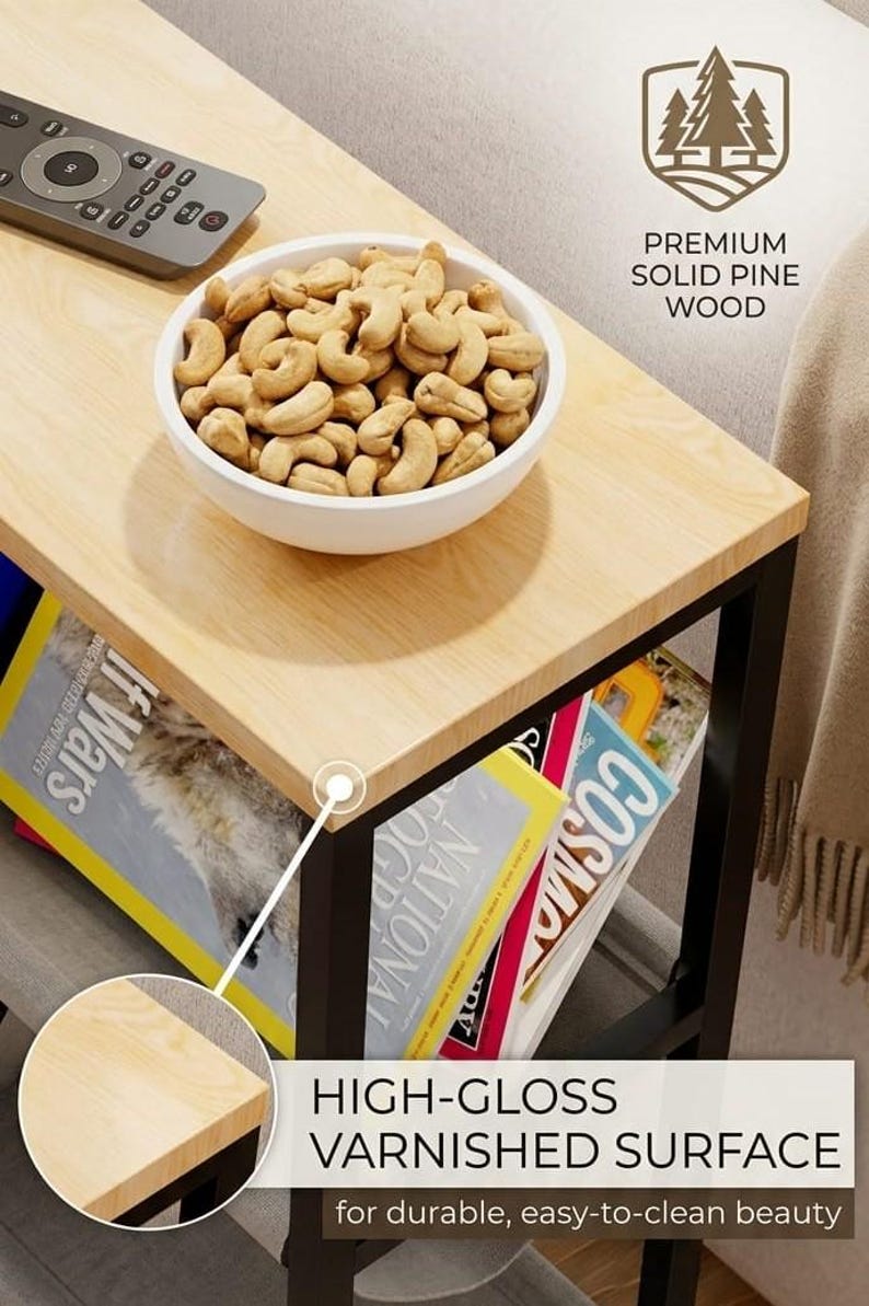 Op de afbeelding: Een licht houten bijzettafel met een zwart metalen frame. Een witte kom gevuld met cashewnoten staat bovenop, naast een afstandsbediening. Tijdschriften worden op de plank eronder bewaard. De tekst luidt "HIGH-GLOSS VARNISHED SURFACE".