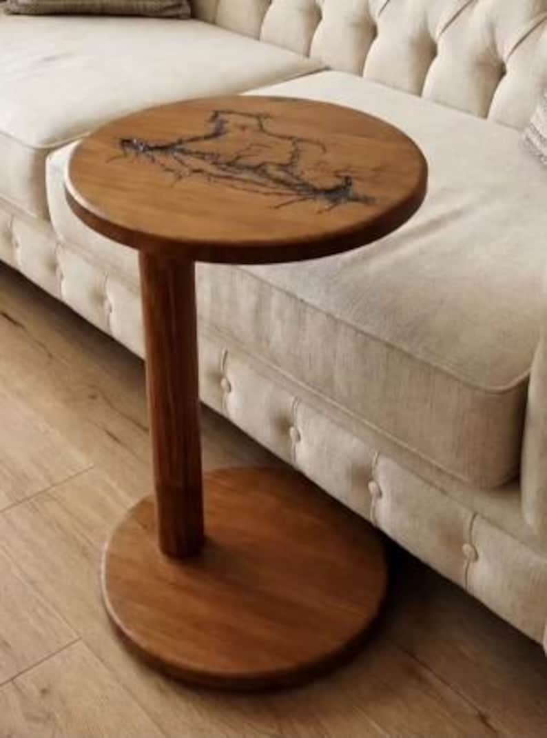 Pode incluir: Uma mesa lateral redonda de madeira com uma &uacute;nica coluna de suporte cil&iacute;ndrica e uma base circular. O tampo apresenta um acabamento de gr&atilde;o de madeira natural com uma incrusta&ccedil;&atilde;o de resina escura ramificada que cria um padr&atilde;o org&acirc;nico.
