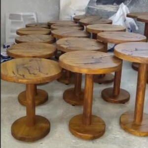 Pode incluir: Uma cole&ccedil;&atilde;o de pequenas mesas laterais redondas de madeira com acabamento castanho natural. Cada mesa apresenta uma base de pedestal central cil&iacute;ndrica e um tampo circular com veios de madeira vis&iacute;veis e detalhes de fissuras escuras.