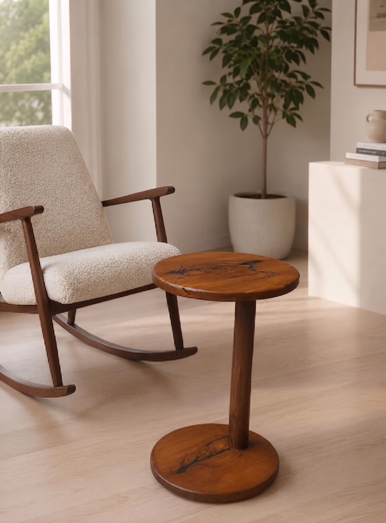 Pode incluir: Uma mesa lateral redonda de madeira com acabamento de gr&atilde;o natural e incrusta&ccedil;&otilde;es de resina escura de formas org&acirc;nicas no topo e na base. A mesa possui uma coluna central cil&iacute;ndrica que liga o tampo circular &agrave; base circular.