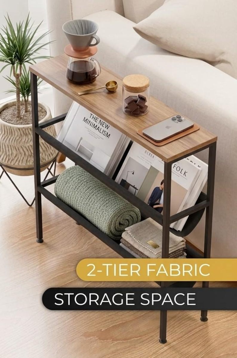 Op de afbeelding: Een bijzettafel met twee niveaus, met een houten blad en een zwart metalen frame. De bovenste plank bevat een koffiezetapparaat, een klein potje en een telefoon. De onderste plank bevat opgerolde dekens en boeken. De tekst "2-TIER FABRIC STORAGE SPACE" wordt weergegeven.