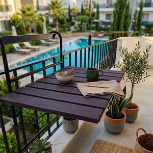 Puede incluir: Una mesa de balcón plegable de color marrón oscuro con un marco de metal negro. La mesa tiene un cuenco pequeño con lavanda, una taza verde, una servilleta beige y un bolígrafo. También se ven plantas en macetas y una cesta de mimbre, con una piscina al fondo.