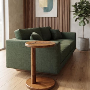 Pode incluir: Uma mesa lateral redonda de madeira com acabamento de gr&atilde;o natural e uma base de pedestal cil&iacute;ndrica &uacute;nica. O tampo da mesa apresenta um detalhe de incrusta&ccedil;&atilde;o escuro de forma org&acirc;nica no centro, sobre uma base circular.