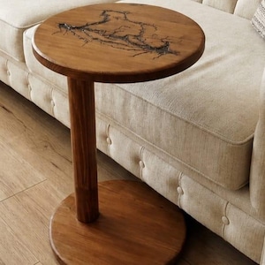 Pode incluir: Uma mesa lateral redonda de madeira com uma base de pedestal cil&iacute;ndrica e uma placa de base circular. O tampo da mesa apresenta um padr&atilde;o de queima fractal escuro e ramificado sobre o veio natural da madeira, com um acabamento liso e polido.