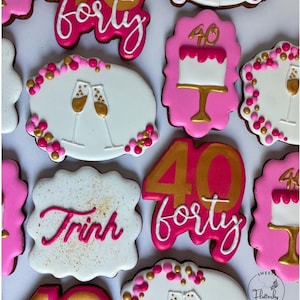 May include: A collection of decorated sugar cookies featuring pink, white, and gold icing. Designs include the number 40, the word forty, champagne flutes, cakes on stands, and the name Trinh, accented with small pink and gold icing dots.