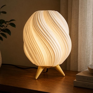 K&ouml;nnte beinhalten: Eine wei&szlig;e Tischlampe mit einem abgerundeten, spiralf&ouml;rmig gerippten Lampenschirm, der ein warmes Licht ausstrahlt. Die Lampe steht auf drei kurzen, hellen, konisch zulaufenden Beinen, die den Hauptk&ouml;rper von der Oberfl&auml;che abheben.