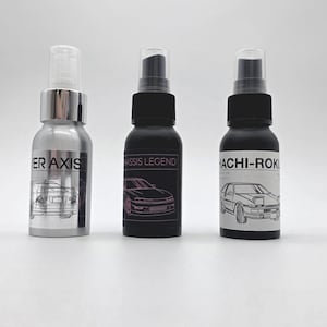 Könnte beinhalten: Drei Sprühflaschen mit transparenten Kappen. Die linke Flasche ist silberfarben mit dem Text "ER AXIS" und einer Autoillustration. Die mittlere Flasche ist mattschwarz mit "CHASSIS LEGEND" und einem Auto. Die rechte Flasche ist mattschwarz mit einem weißen Etikett mit dem Text "HACHI-ROKU" und einem Auto.