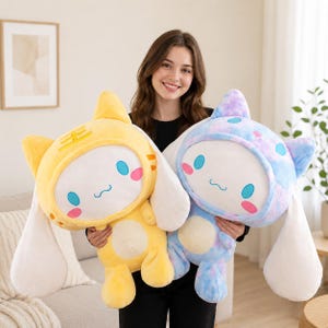 May include: Two plush toys featuring white faces with blue oval eyes and pink cheeks, wearing hoods with long white ears. One plush has a yellow hood with orange stripes, while the other has a blue and purple tie-dye hood with blue spots.