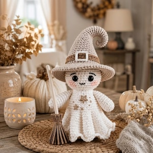 May include: A crocheted doll wearing a beige pointed hat with a brown band and white buckle. The doll has a white dress with embroidered beige stars, black eyes, and pink cheeks. It holds a small wooden broom with brown bristles in its hand.