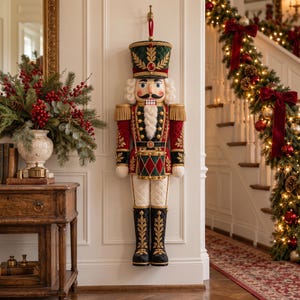 May include: A large wall-hanging nutcracker soldier decoration featuring a green quilted hat, a red and green uniform with gold trim, a white beard, and a small drum. The figure is detailed with gold embroidery and red accents.
