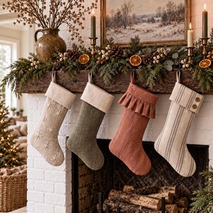 Puede incluir: Cuatro calcetines navideños colgados en una repisa de chimenea. El primero es beige con estrellas bordadas, el segundo es verde oliva con patrón de espiga, el tercero es terracota con puño con volantes y el cuarto es de rayas.