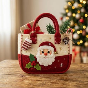 May include: A cream and red felt tote bag featuring a central Santa Claus face appliqué, green holly leaves with red berries, and embroidered white snowflakes. The bag includes a small hanging mitten, a pinecone, and a candy cane decoration.