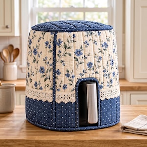 May include: A quilted appliance cover featuring a cream-colored fabric with a blue floral pattern on the top and sides, accented by a white lace trim and a dark blue fabric with white polka dots at the base, with a cutout for a silver handle.