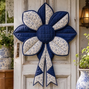 Può includere: Un arazzo in tessuto trapuntato a forma di grande fiore con otto petali. Il design alterna il blu navy a tinta unita e un tessuto bianco con un piccolo motivo floreale blu. Un pezzo centrale circolare trapuntato blu navy si trova al centro.