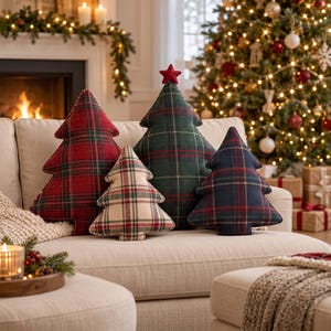 May include: Four Christmas tree-shaped cushions in various sizes and plaid patterns. One is red, one is dark green with a red star on top, one is cream with red and green lines, and one is dark blue. All feature a classic tartan check design.