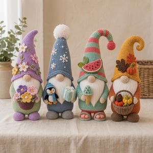 Op de afbeelding: Vier gehaakte kabouterfiguren op een rij. De eerste draagt een lavendelkleurige muts met bloemen en houdt een mandje met bloemen vast. De tweede heeft een blauwe muts met sneeuwvlokken, met een pinguïn en een cadeau. De derde heeft een gestreepte muts met een watermeloen en houdt een ijsje vast. De vierde draagt een oranje muts met bladeren en een pompoen, met een mandje vol herfstproducten.