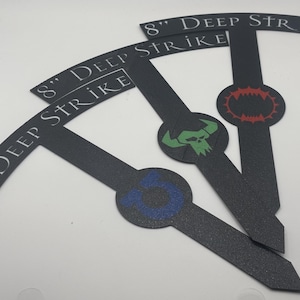 May include: Black, textured game markers with the text "8" DEEP STRIKE". Each marker has a different colored emblem: blue, green skull, and red. The markers are approximately 20 cm long.