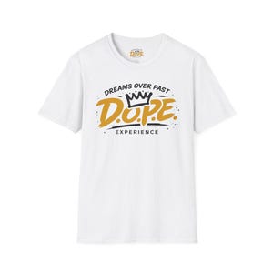 Puede incluir: Camiseta blanca con la palabra "D.O.P.E." en letras doradas y negras, con un gráfico de corona encima. El texto "DREAMS OVER PAST EXPERIENCE" está encima y debajo de la palabra "D.O.P.E."