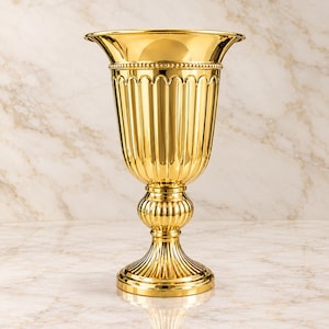 Könnte beinhalten: Eine glänzende goldfarbene Metallvase mit einem breiten, ausgestellten Rand und einer Perlenkante. Der Körper der Vase weist vertikale Rillen, ein abgerundetes Mittelstück und einen runden Sockel auf, alles mit einer hochglänzenden, polierten Oberfläche.