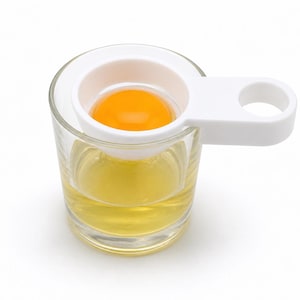May include: A clear glass filled with egg whites, with a bright orange egg yolk separated in a white egg separator. The separator has a handle for easy use. The egg separator is placed over the glass.